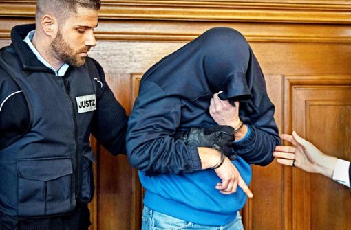Der Angeklagte im Fall des  Dreifachmordes von Villingendorf wird in den Saal des Rottweiler Landgerichts geführt. Um nicht erkannt zu werden, zieht er sich seine Jacke über den Kopf. Foto: dpa