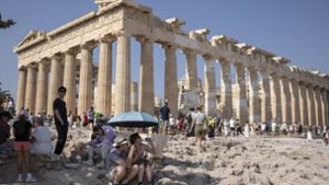 Eine Touristin trinkt Wasser, während sie und ein Mann unter einem Regenschirm vor dem Parthenon-Tempel auf dem Akropolis-Hügel in Athen Schutz vor der Sonne suchen. Am Wochenende werden in Griechenland und auf Zypern, aber auch im Westen der Türkei Höchsttemperaturen von über 40 Grad erwartet. Foto: AP/dpa/Petros Giannakouris
