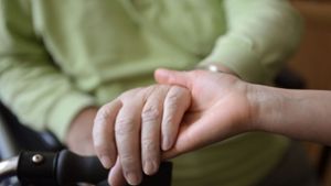 Eine junge Frau hält in einem Seniorenpflegeheim die Hände eines alten Mannes. Foto: dpa/Jens Kalaene