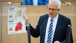 Ministerpräsident Winfried Kretschmann im Landtag mit zwei Karten, die die Entwicklung des Infektionsgeschehens innerhalb von wenigen Wochen dokumentieren. Foto: dpa/Sebastian Gollnow