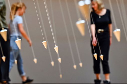 Zwei Besucherinnen erkunden im ZKM William Forsythes Installation „Nowhere and Everywhere at the Same Time No. 2” und laufen zwischen schwingenden Pendeln. Foto: dpa/Uli Deck