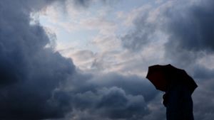 Ein Mann geht mit einem Regenschirm vor aufziehenden dunklen Wolken spazieren. Foto: dpa/Martin Gerten