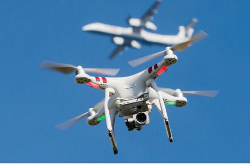 Eine Quadrocopter-Drohne fliegt in knapp zehn Metern Flughöhe über einem Garten, während in weiter Entfernung ein Flugzeug beim Anflug auf den Flughafen Düsseldorf zu sehen ist. Nach Angaben der Deutschen Flugsicherung sind deutsche Flughäfen bei Drohnenattacken nur bedingt abwehrbereit. Foto: dpa