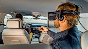 Ein Passagier mit einer VR-Brille sitzt auf der Rückbank eines Audi. Das Fahrzeug ist mit einer Plattform ausgestattet, mit der Virtual-Reality-Filme, Videospiele und interaktive Inhalte realistisch erlebt und  in Echtzeit an die Fahrbewegungen des Autos anpasst werden können. Foto: Audi