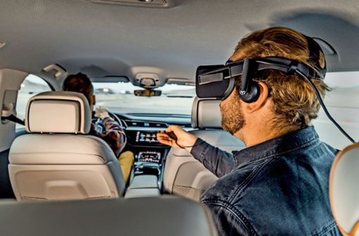Ein Passagier mit einer VR-Brille sitzt auf der Rückbank eines Audi. Das Fahrzeug ist mit einer Plattform ausgestattet, mit der Virtual-Reality-Filme, Videospiele und interaktive Inhalte realistisch erlebt und  in Echtzeit an die Fahrbewegungen des Autos anpasst werden können. Foto: Audi
