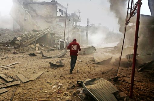 Ein Mitarbeiter des Syrischen Roten Halbmondes eilt durch ein Viertel von Ost-Ghuta nahe Damaskus im Rebellengebiet, das von Angriffen der Luftwaffe getroffen wurde. Foto: dpa