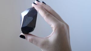 Eine Mitarbeiterin von Sotheby’s Dubai hält den 555,55 Karat schweren Schwarzen Diamanten „The Enigma“ in der Hand, der in der Galerie von Sotheby’s Dubai versteigert werden soll. Foto: dpa/Kamran Jebreili