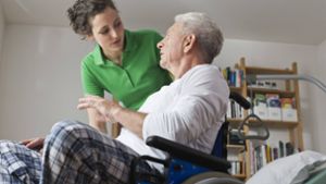 Eine Pflegerin unterstützt einen älteren Mann im Rollstuhl. Foto: Westend61/imago