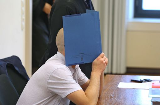 Der Angeklagte sitzt in einem Gerichtssaal im Landgericht in Memmingen auf der Anklagebank und verdeckt dabei mit einem Aktendeckel sein Gesicht. Foto: dpa