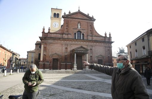Zwei Männer Menschen mit Mundschutz stehen vor der Kirche San Biagio. In Italien soll die weitere Ausbreitung des Coronavirus mit drastischen Mitteln bekämpft werden. Foto: dpa/Luca Bruno