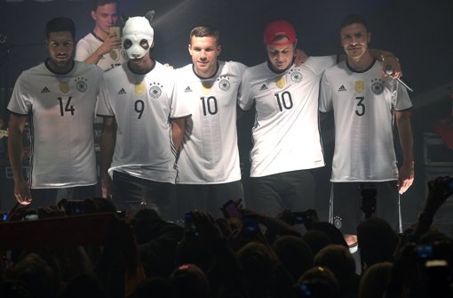 Die Fußballnationalspieler Emre Can (links), Lukas Podolski (Mitte) und Jonas Hector (rechts) posieren mit Rapper Cro in den neuen Leibchen. Foto: dpa