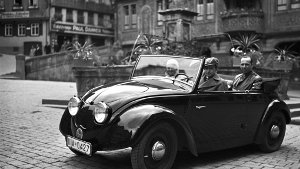Das Werksfoto aus dem Jahr 1936 zeigt Ferry Porsche am Steuer des zweiten Volkswagen-Prototypen (V2), fotografiert auf dem Marktplatz in Tübingen. Neben ihm seine Frau Dorothea. Auf dem Rücksitz Hellmuth Zarges, ein Freund der Familie Porsche. Foto: Porsche Werksfoto/dpa