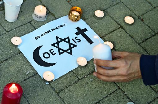 Ein Mann entzündet während einer Mahnwache vor der Fatih Camii Moschee im sächsischen Dresden  eine Kerze neben einem Schild mit der Aufschrift „Coexist“ und religiösen  Symbolen von Islam, Judentum und Christentum. Foto: Sebastian Kahnert/dpa