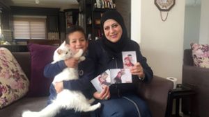 Sohn Madschd (5) und Lydia Rimawi (42) sitzen in ihrem Wohnzimmer auf dem Sofa. In ihren Händen hält Lydia Bilder von sich und ihrem Ehemann Foto: dpa