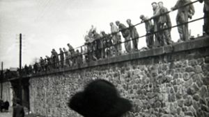 Unten gehen Passanten, oben am Rand der Bahnstrecke stehen KZ-Häftlinge. Foto: BR