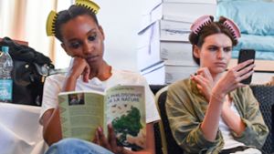 Zwei Models lesen während der Berliner Fashion Week in einem Buch und auf einem Smartphone. Foto: dpa