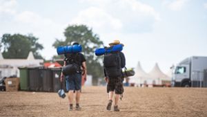 Zwei Festivalbesucher gehen mit ihrem Reisegepäck über das Wacken Open Air Festival. Foto: dpa/Daniel Reinhardt