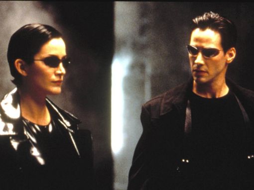 Schwarze Leder-Outfits und Sonnenbrillen: Carrie-Anne Moss und Keanu Reeves in Matrix. Foto: imago images/Everett Collection/Warner Bros.