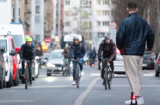 Ein junger Mann fährt auf einem E-Scooter eine Straße in Stuttgart entlang, während ihm drei Fahrradfahrer entgegenkommen Foto: dpa/Gregor Bauernfeind