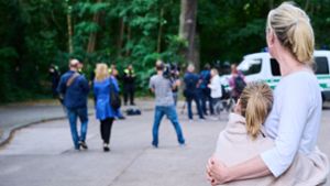 Eine Anwohnerin und ihre Tochter sehen dem Treiben von Journalisten und Polizei zu, während Tierexperten und Polizeibeamten in einem Waldgebiet in Zehlendorf stehen. Foto: dpa/Annette Riedl