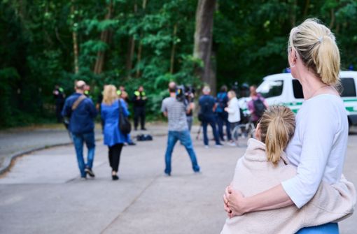 Eine Anwohnerin und ihre Tochter sehen dem Treiben von Journalisten und Polizei zu, während Tierexperten und Polizeibeamten in einem Waldgebiet in Zehlendorf stehen. Foto: dpa/Annette Riedl