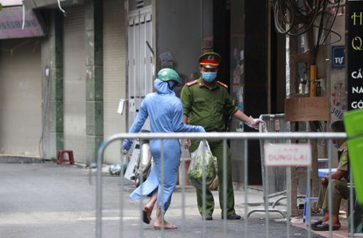 Eine Frau geht vor einem Supermarkt an einem Polizisten mit Mundschutz vorbei. Vietnam verschärft die Corona-Maßnahmen, da die Zahl der lokalen Infizierten seit dem Wochenende zunimmt. Foto: dpa/Hau Dinh