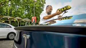 Ahmet Gül befestigt sein Taxischild auf seinem Tesla: Nun ist er bereit, seine Kunden elektrisch von A nach B zu fahren. Foto: Lichtgut/Julian Rettig