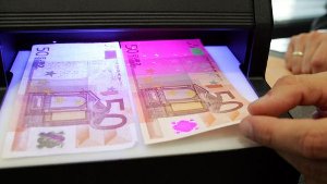 Unter einem UV-Lichtgerät lassen sich Banknoten auf Echtheit prüfen. Links liegt der falsche, rechts der echte 50-Euro-Schein. Foto: AP