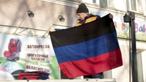 Ein Gemeindearbeiter hält eine Flagge der international nicht anerkannten Volksrepublik Donezk, die an einem Gebäude in der gleichnamigen Stadt angebracht werden soll. (Archivbild) Foto: dpa/Alexei Alexandrov