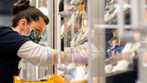 Ein Mitarbeiterin in einem Supermarkt bestückt mit Mundschutz vor Ladenöffnung ein Regal. Foto: dpa/Robert Michael