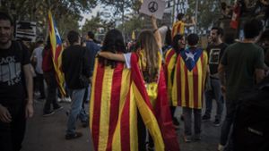 Zwei Frauen, eine trägt die Unabhängigkeitsflagge Kataloniens um ihre Schultern (l), die andere eine spanische Nationalflagge und hält dabei ein „Peace“-Zeichen hoch, laufen durch die Straßen von Barcelona. Foto: AP