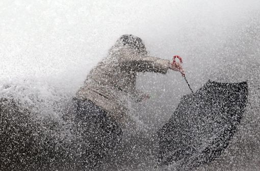 Eine Frau versucht mit ihrem Regenschirm gegen eine Welle anzukämpfen, die den Hafendamm Biarritz vor der Atlantikküste erreicht. In Südwestfrankreich hat der Wintersturm „Fabien“ Geschwindigkeiten von bis zu 150 Stundenkilometern erreicht. Foto: dpa/Bob Edme