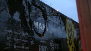 Der Bus von Borussia Dortmund steht mit einer beschädigten Scheibe an einer Straße. Foto: dpa