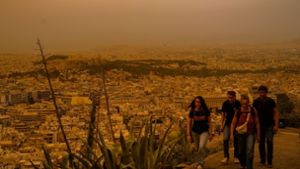 Touristen spazieren auf dem Lycabettus-Hügel in Athen, während der Himmel über der griechischen Hauptstadt mit dem antiken Akropolis-Hügel im Hintergrund infolge von Saharastaub eingetrübt ist. Foto: Petros Giannakouris/AP/dpa
