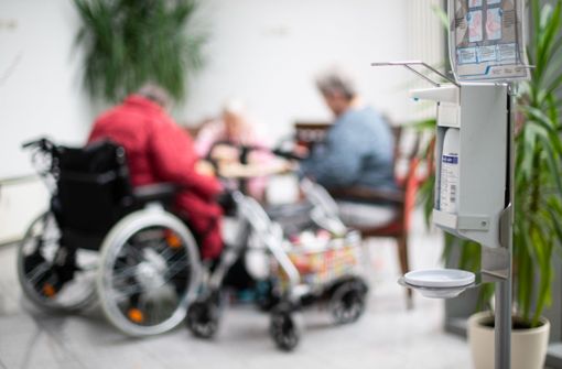 Ein Desinfektionsmittelspender hängt in einem Altenheim, im Hintergrund sitzen Seniorinnen. Foto: dpa/Jonas Güttler