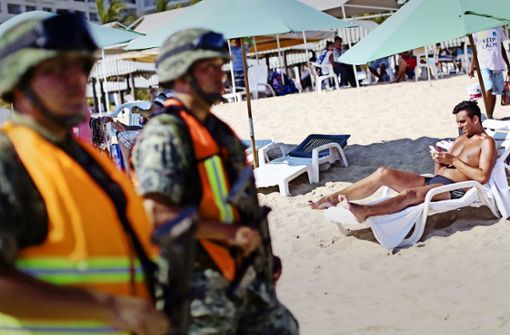 Schwerbewaffnete Polizisten bewachen Badende am Strand von Acapulco: das einstige Urlauberparadies ist wegen eines Bandenkriegs nicht mehr sicher. Foto: AFP