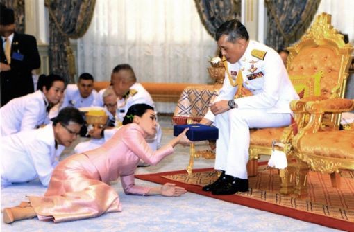 Andere Länder, andere Sitten: König Maha Vajiralongkorn (M) überreicht seiner auf dem Boden liegenden Ehefrau Suthida ein Geschenk. Foto: dpa