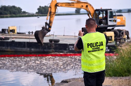 Ein Polizist macht ein Foto eines Baggers der tote fische aus der Oder bei Krajnik Dolny in Polen schaufelt. Foto: dpa/Marcin Bielecki