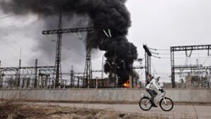 Nach einem russischen Angriff fährt ein Mann mit seinem Rad an einem brennenden Elektrizitätswerk in Charkiw vorbei. Foto: Yevhen Titov/AP/dpa
