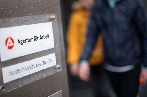 Stuttgart: Zwei Männer gehen hinter dem Logo der Agentur für Arbeit vorbei. Foto: dpa/Sebastian Gollnow