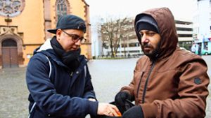 Fatih Ceylan steckt einem Obdachlosen vor der Leonhardskirche eine Orange in den Rucksack. Foto: Tilman Baur
