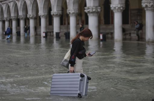 Überschwemmungen in Venedig. Eine Frau wartet mit ihrem Koffer durch das Wasser auf dem Markusplatz. Foto: dpa/Luca Bruno