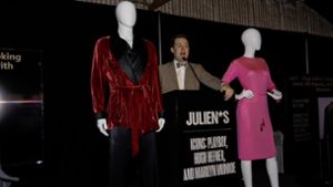 Ein Auktionator  bietet Hugh Hefners Smoking-Jacket und Marilyn Monroes rosa Pucci-Kleid bei der Versteigerung in Los Angeles zum Verkauf an. Foto: -/Julien’s Auctions/dpa