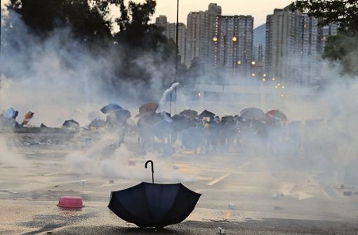 Ein Regenschirm liegt auf einer Straße, während Demonstranten vor Tränengas in Deckung gehen. Foto: picture alliance/dpa/Kin Cheung