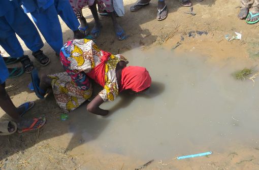 Ein durstiges Mädchen trinkt im Lager Muna Garage in Maiduguri, Nigeria, aus einer verdreckten Pfütze Wasser. Foto: dpa