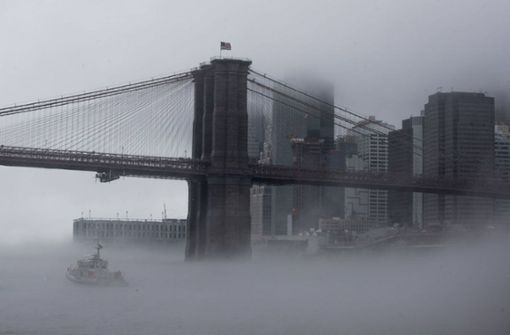 Ein Boot der New Yorker Polizei fährt  unter der Brooklyn Bridge durch  dichten Nebel. Foto: dpa