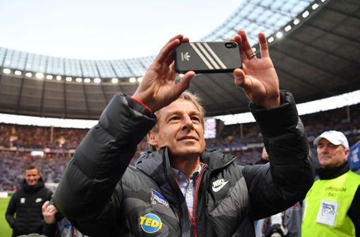Jürgen Klinsmann filmt mit seinem Smartphone vor dem Spiel im Stadion von Hertha BSC Berlin. Foto: Bernd König/Bernd König