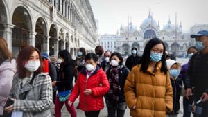 Kein Maskenball: Touristen aus Asien versuchen, sich vor Ansteckung zu schützen, während sie über den Piazza San Marco in Venedig hasten. Foto: AFP/Andrea Pattaro